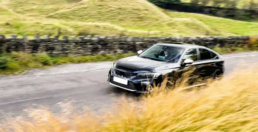 Rechtsgelenktes schwarzes Auto auf Landstraße durch grüne Wiesen