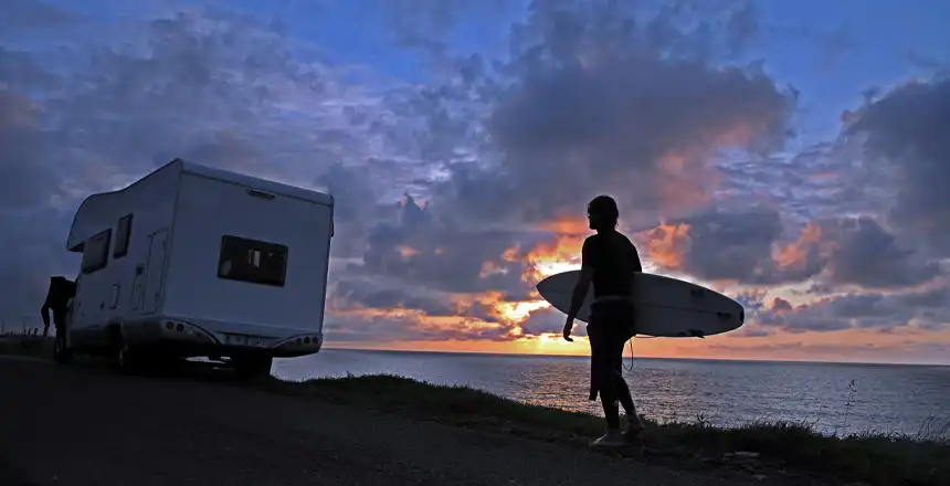 Surfer mit Brett in der D&auml;mmerung geht zu seinem Wohnmobil